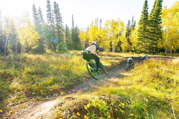 Three mountain bikers ride a fast trail at dusk on a trail in Park City, UT