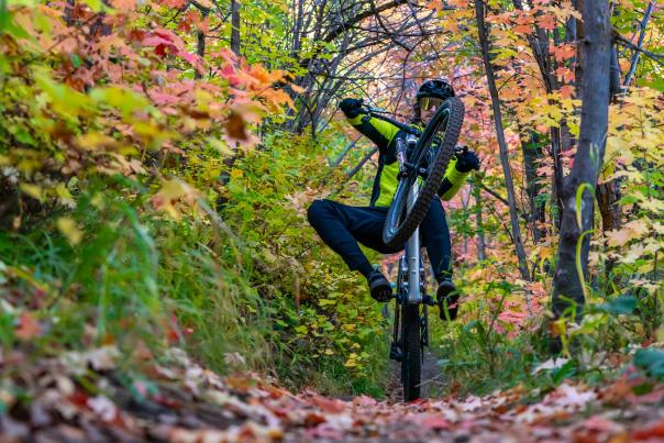 A mountain biker wheelies on a trail surrounded by colorful fall leaves in Park City, UT