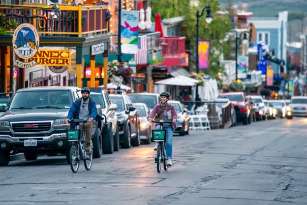 Two bikers ride up Main Street Park City at dusk on electric cruiser bikes