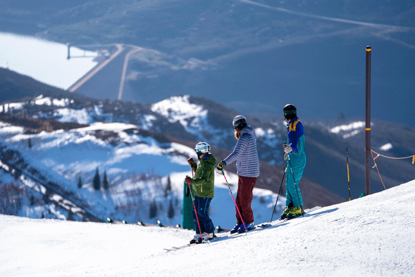 Three skiers look down a steep ski run on a sunny day at Deer Valley Resort in Park City, UT