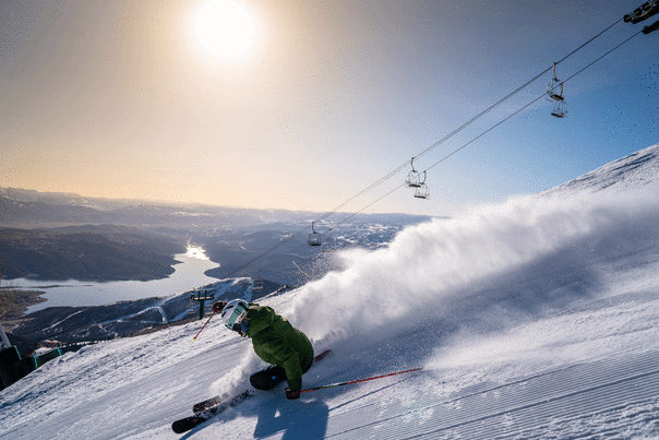 A skier carves a turn on groomed ski run overlooking a reservoir on a sunny day at Deer Valley in Park City, UT