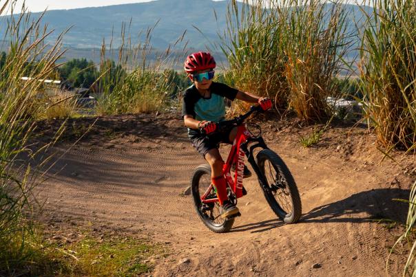 A young boy riding a red bike rounds a berm turn on a pump track at the Trailside Bike Park in Park City, UT