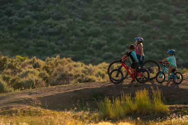 A woman and two children observe riding features on a sunlit trail in Park City, UT