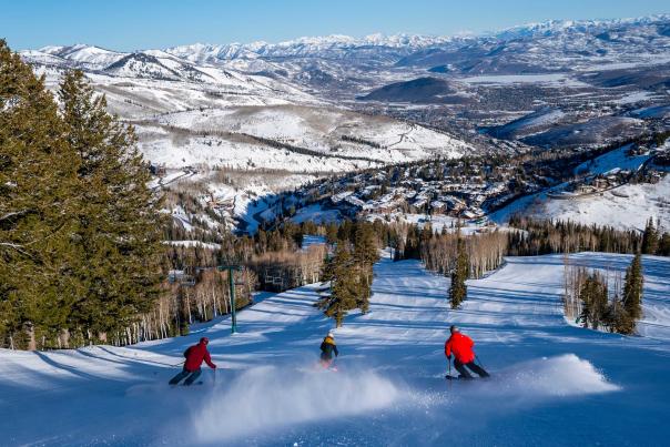 Three skiers descend a freshly groomed run on a sunny winter day at Deer Valley Resort in Park City, UT