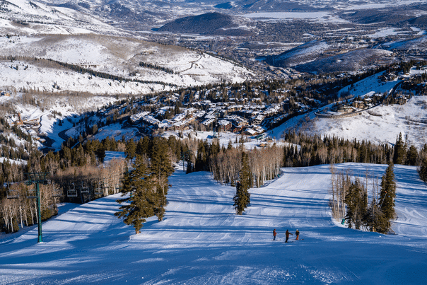 Three skiers talk as a group on a groomed run on a sunny day at Deer Valley Resort in Park City, UT