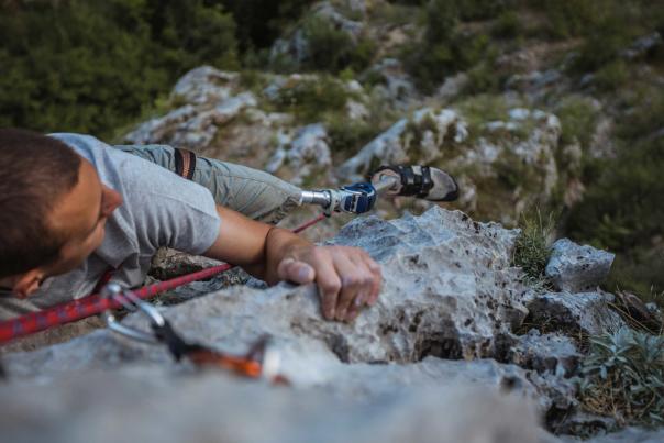 An adaptive climber scales a steep cliff face using ropes and belays