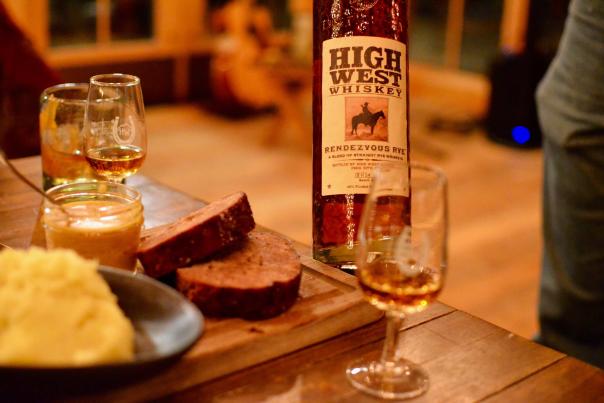 A whiskey tasting glass set on a wood table with food and a bottle of High West Whiskey at a restaurant in Park City, UT