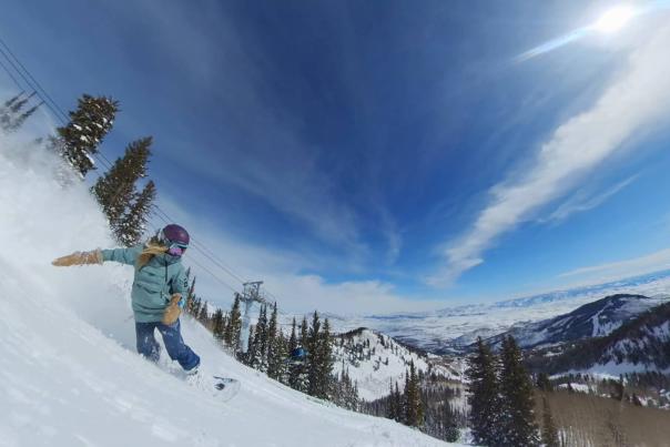 A snowboarder carves in powder sun on a sunny day in Park City, UT