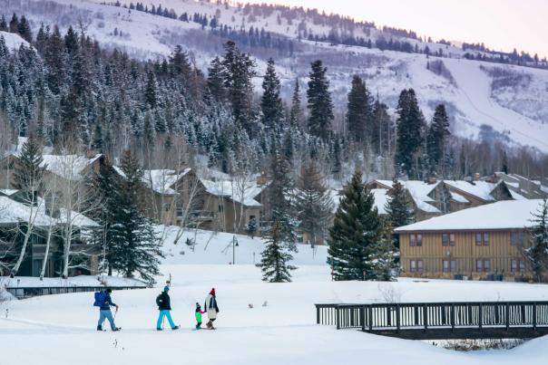 A family of four and a guide snowshoe towards a wooden bridge at sunset in Park City, UT