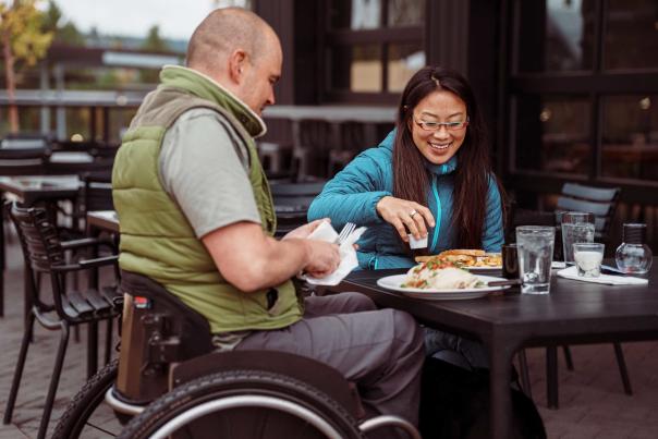A person in a wheelchair eats a meal with another person on an outdoor deck at a restaurant in Park City, UT