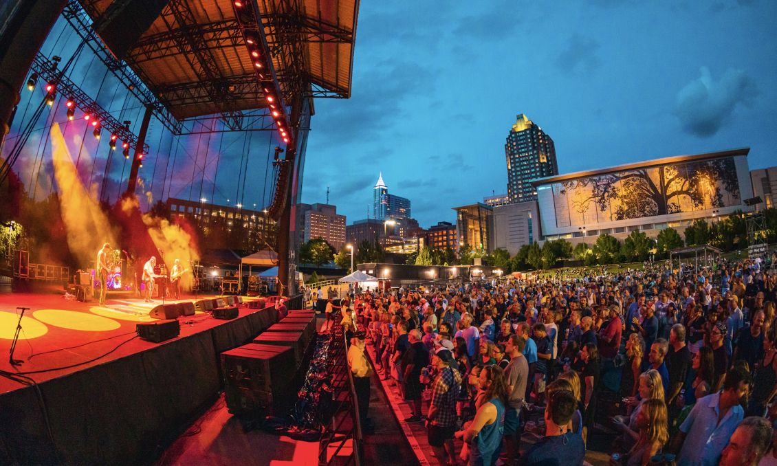 Large crowd at outside amphitheater concert with Raleigh skyline in background