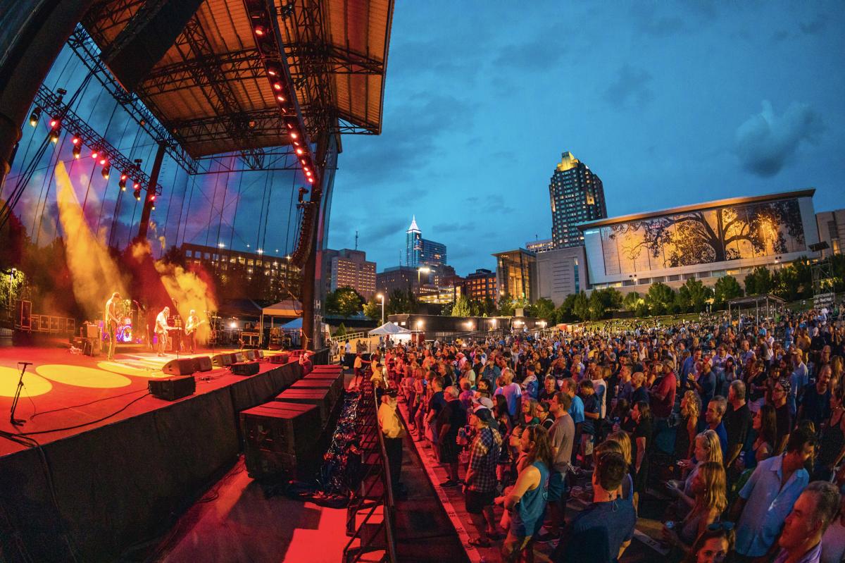 Large crowd at outside amphitheater concert with Raleigh skyline in background