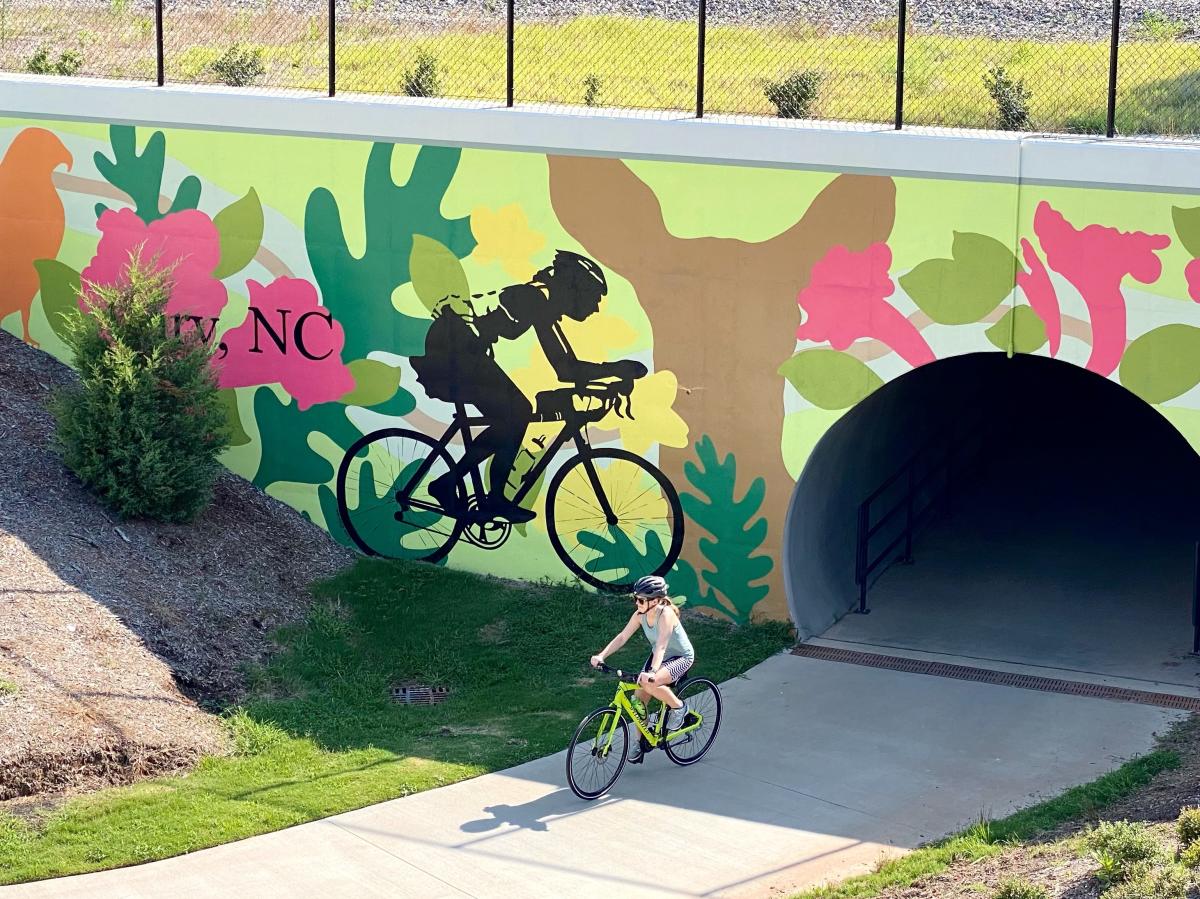 Cyclist comes out of tunnel in front of bicycle mural on Cary greenway