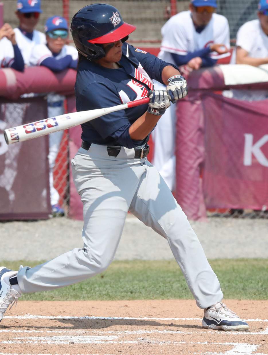 USA women’s baseball player swinging at a pitch during a game.
