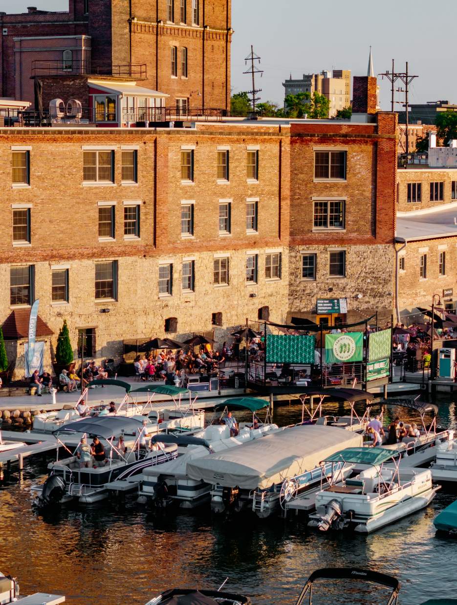 Lively marina in Rockford at sunset with boats docked near a historic brick building and people enjoying the outdoor atmosphere.
