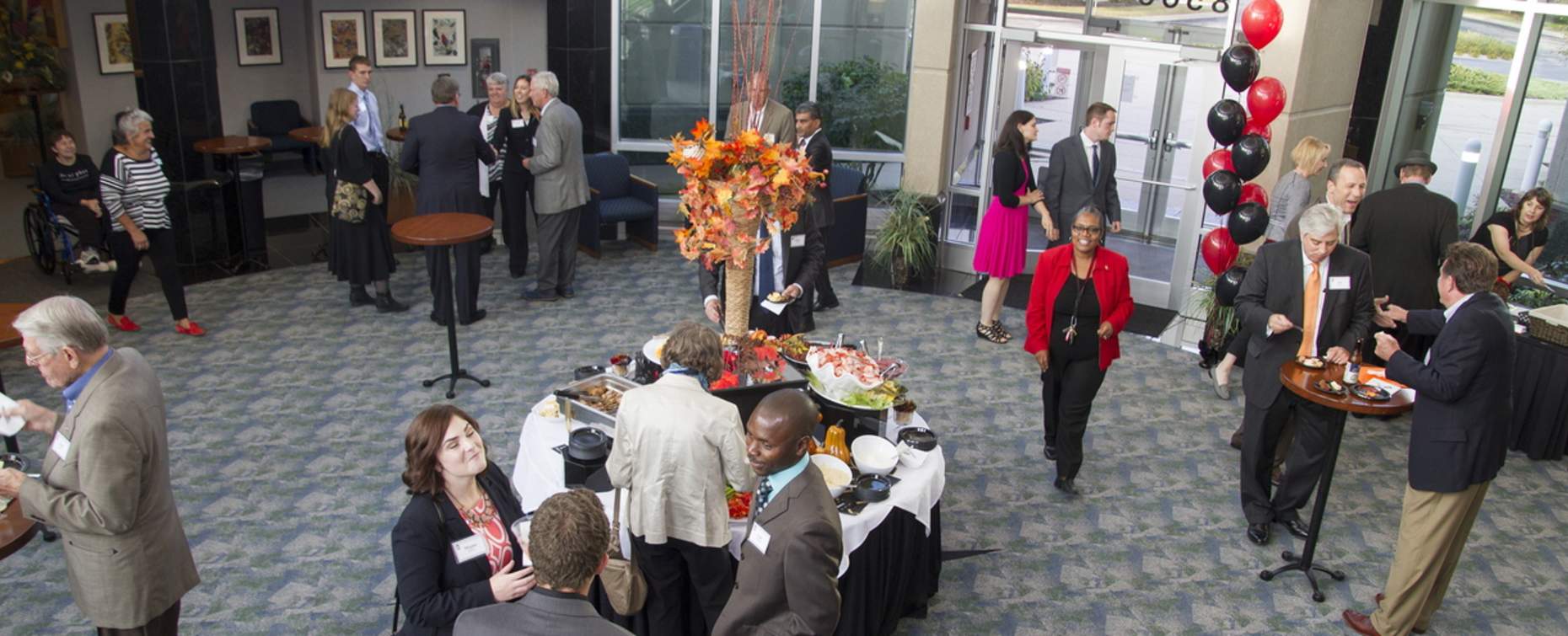 People networking and enjoying food at a Rockford Meeting event with autumn-themed centerpiece and red and black balloons.