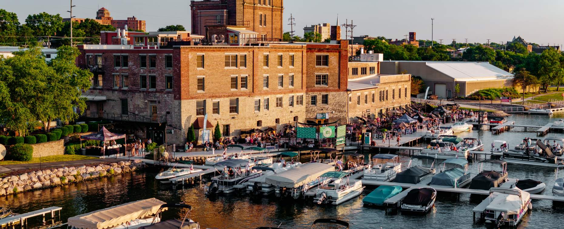 Lively marina in Rockford at sunset with boats docked near a historic brick building and people enjoying the outdoor atmosphere.