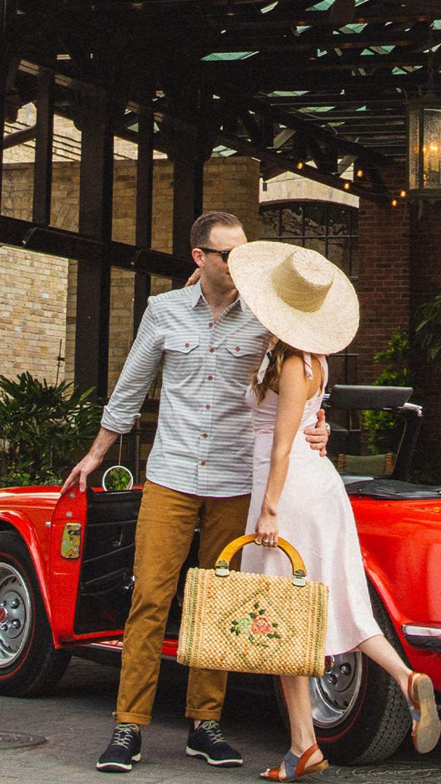 Woman in large hat and man embracing in front of Hotel Emma in San Antonio.