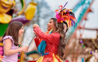 Costumed performer placing beads over girl's head at Six Flags Fiesta Texas' Mardi Gras Festival.