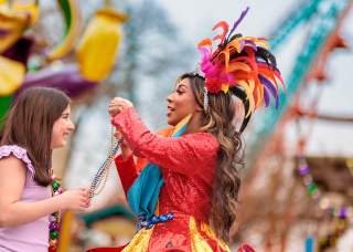 Costumed performer placing beads over girl's head at Six Flags Fiesta Texas' Mardi Gras Festival.