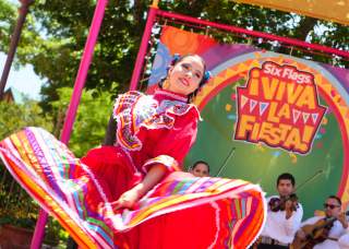 Folklorico dancer in red dress dancing with mariachi band behind her.