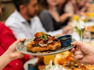 Hands passing eachother a plate of gourmet waffles.
