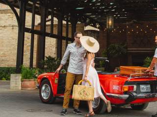 Woman in large hat and man embracing in front of Hotel Emma in San Antonio.