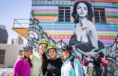 Group of girls wearing bike helmets in front of mural of woman