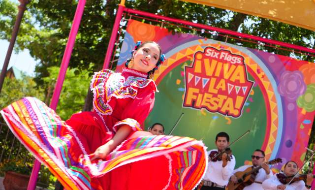 Folklorico dancer in red dress dancing with mariachi band behind her.