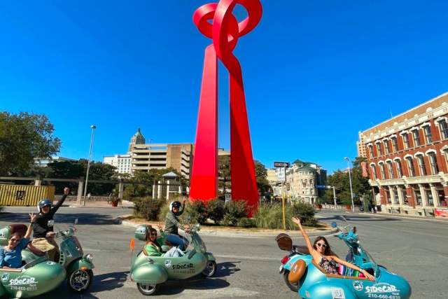 Three sidecar tours driving in front of San Antonio's Torch of Friendship sculpture