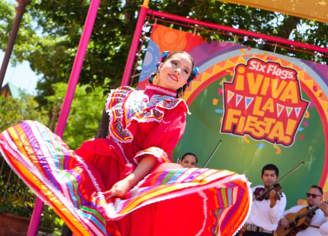 Folklorico dancer in red dress dancing with mariachi band behind her.