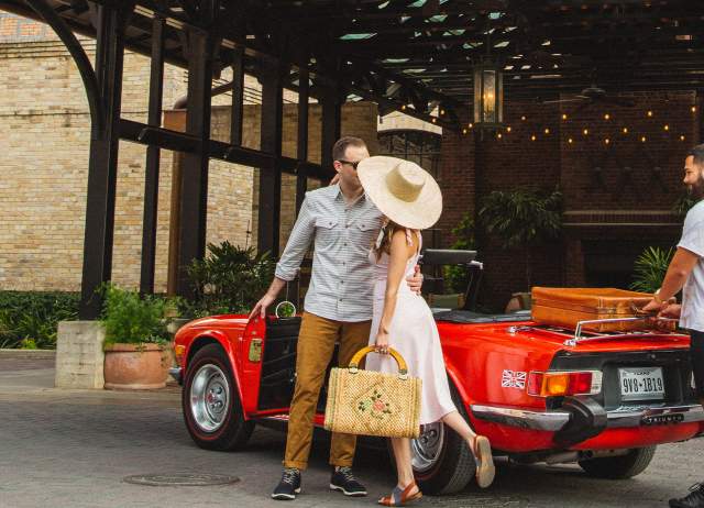 Woman in large hat and man embracing in front of Hotel Emma in San Antonio.