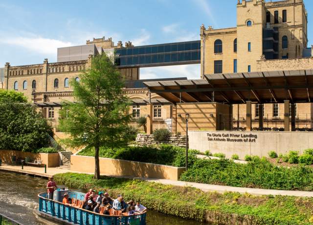 River barge drifting along river in front of San Antonio Museum of Art