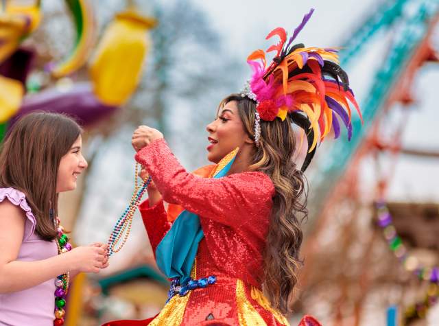 Costumed performer placing beads over girl's head at Six Flags Fiesta Texas' Mardi Gras Festival.