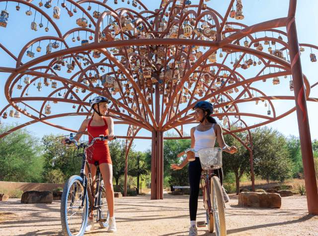 Two girls in front of public art on bikes at Mission Reach in San Antonio.