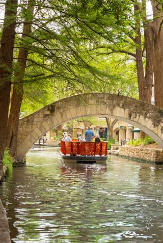 Red GO RIO River barge floating under bridge on San Antonio River Walk.