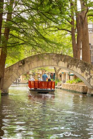 Red GO RIO River barge floating under bridge on San Antonio River Walk.