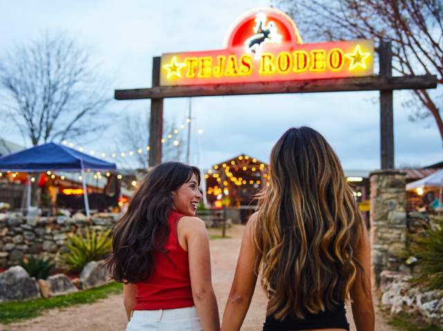Two girls walking under neon sign that reads "Tejas Rodeo."