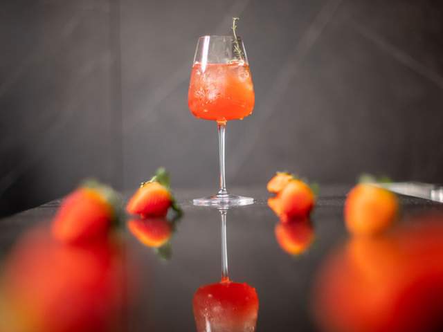 Red drink in wine glass surrounded by strawberries.