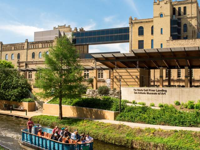 River barge drifting along river in front of San Antonio Museum of Art