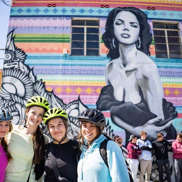 Group of girls wearing bike helmets in front of mural of woman