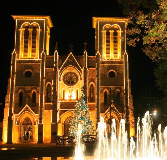San Fernando Cathedral lit up with white Christmas lights and a lit-up water fountain in front of it.