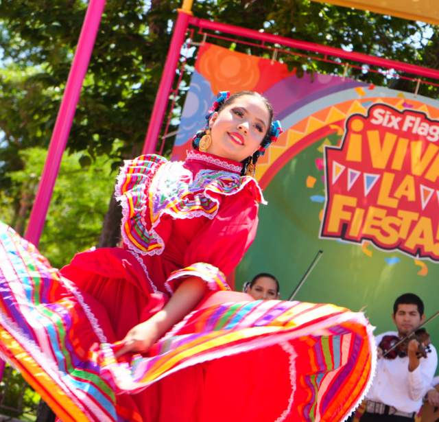 Folklorico dancer in red dress dancing with mariachi band behind her.