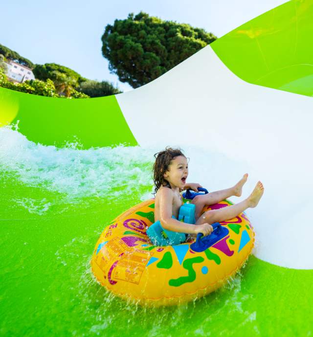 Child on inner tube on waterslide laughing.
