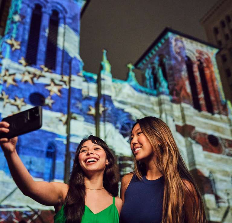 Two girls standing in front of the nightly light show at San Fernando Cathedral in San Antonio.