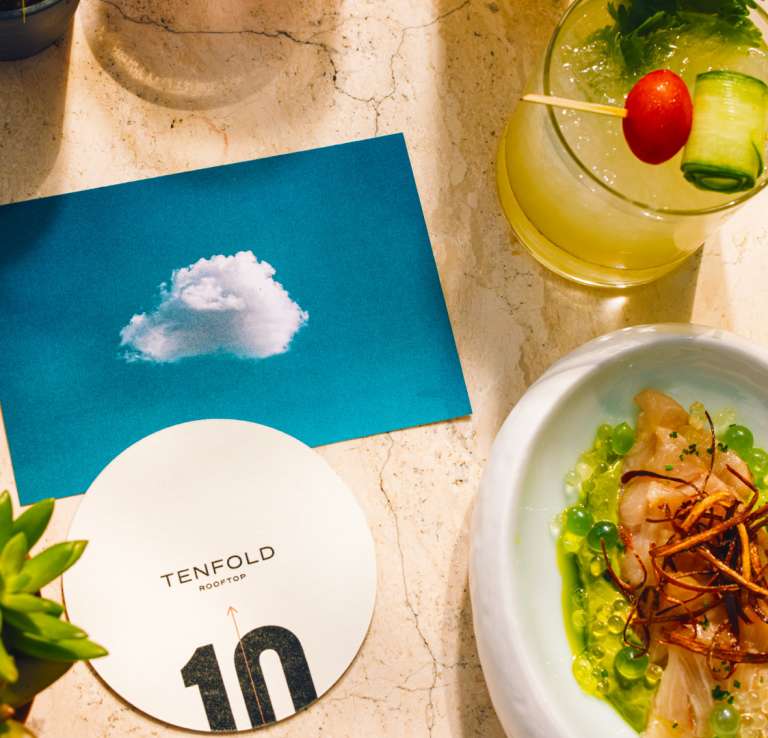 Overhead view of food and drink spread with a coaster from Tenfold Rooftop bar.