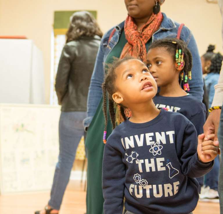 Small child holding parent's hand with photo of MLK in background at DreamWeek San Antonio.
