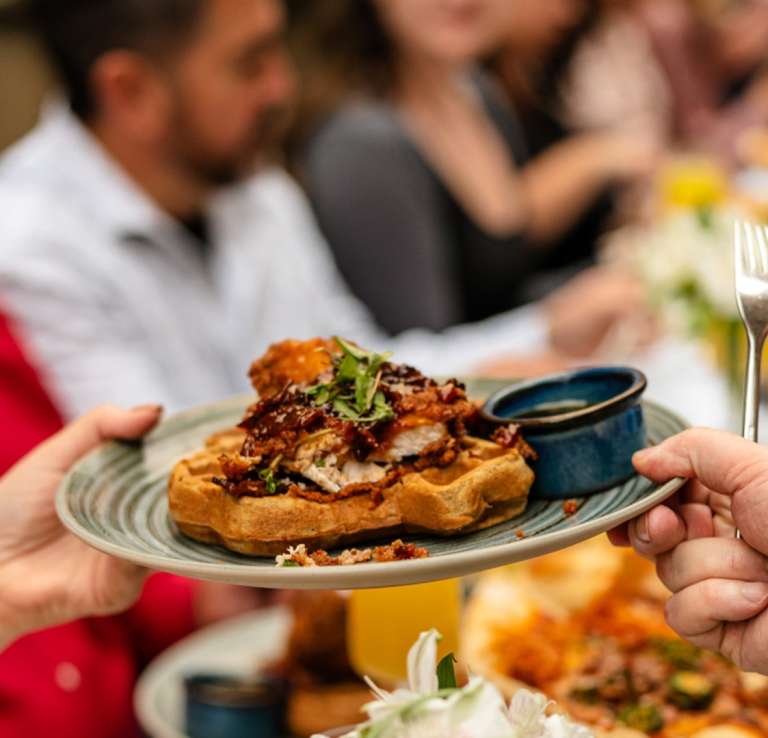 Hands passing eachother a plate of gourmet waffles.
