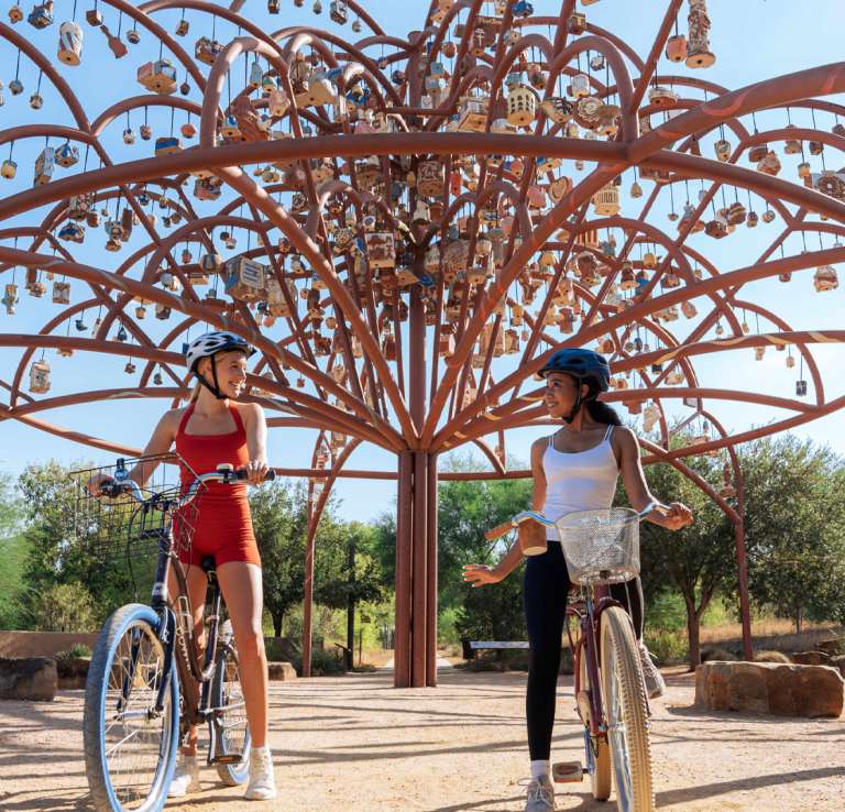 Two girls in front of public art on bikes at Mission Reach in San Antonio.