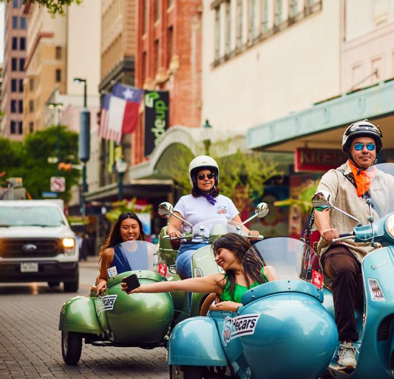 SiDECARS SA Vespa with driver and rider cruising in San Antonio.